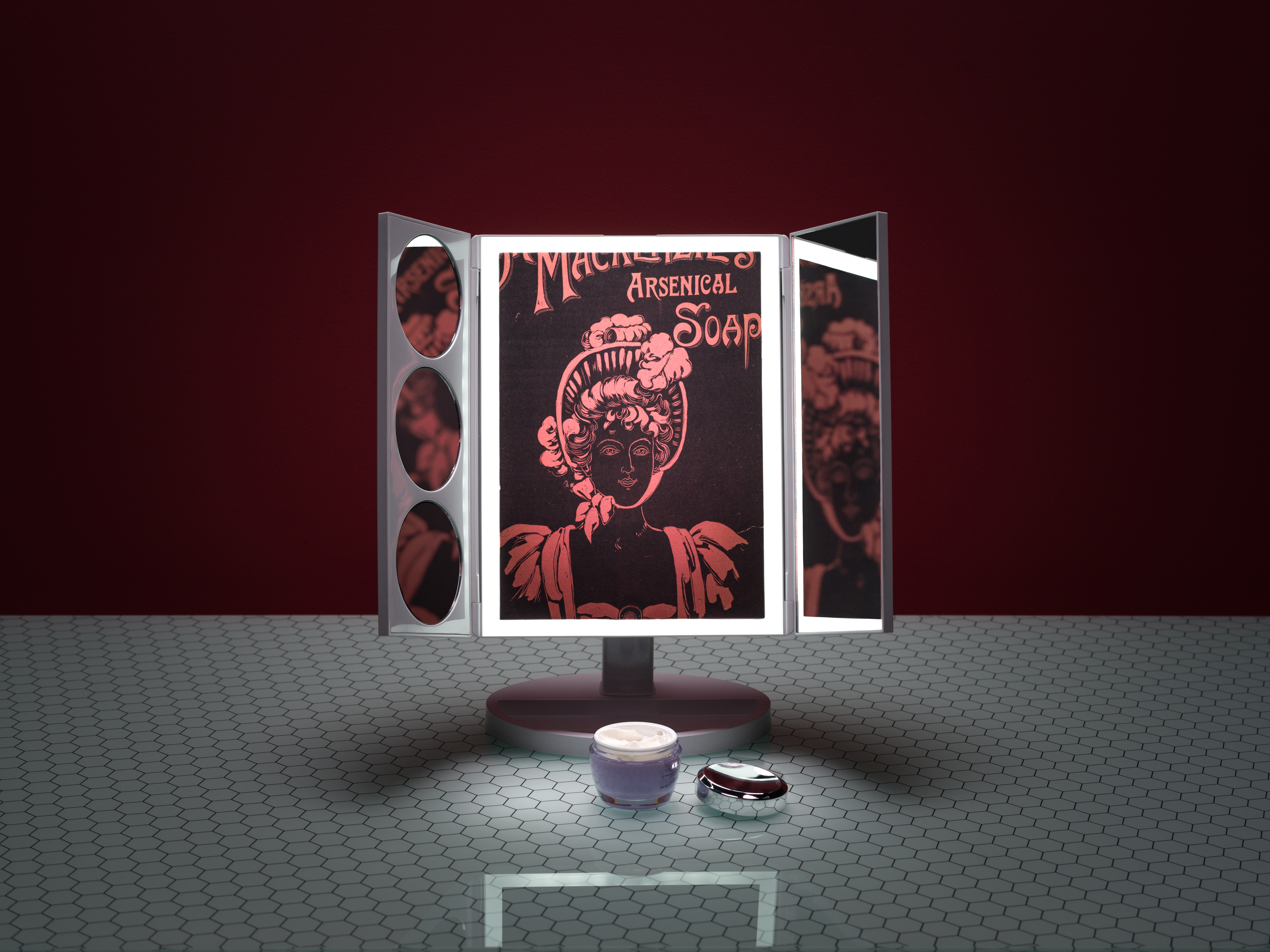 Photograph of a three-fold table beauty mirror with built-in light on a glass patterned tabletop, against a dark red background. On the table in front of the mirror is an open jar of face cream. In the reflections of the mirror an old advertisement for Dr. Mackenzie's Arsenical Soap, be seen.