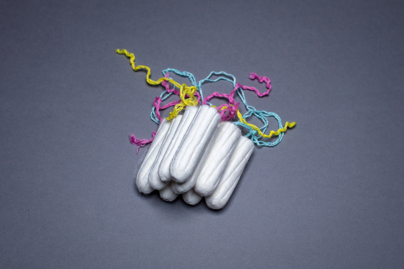 Photograph of a stack of unwrapped tampons against a blue background. The yellow, pink and blue cords are visible behind the stack.