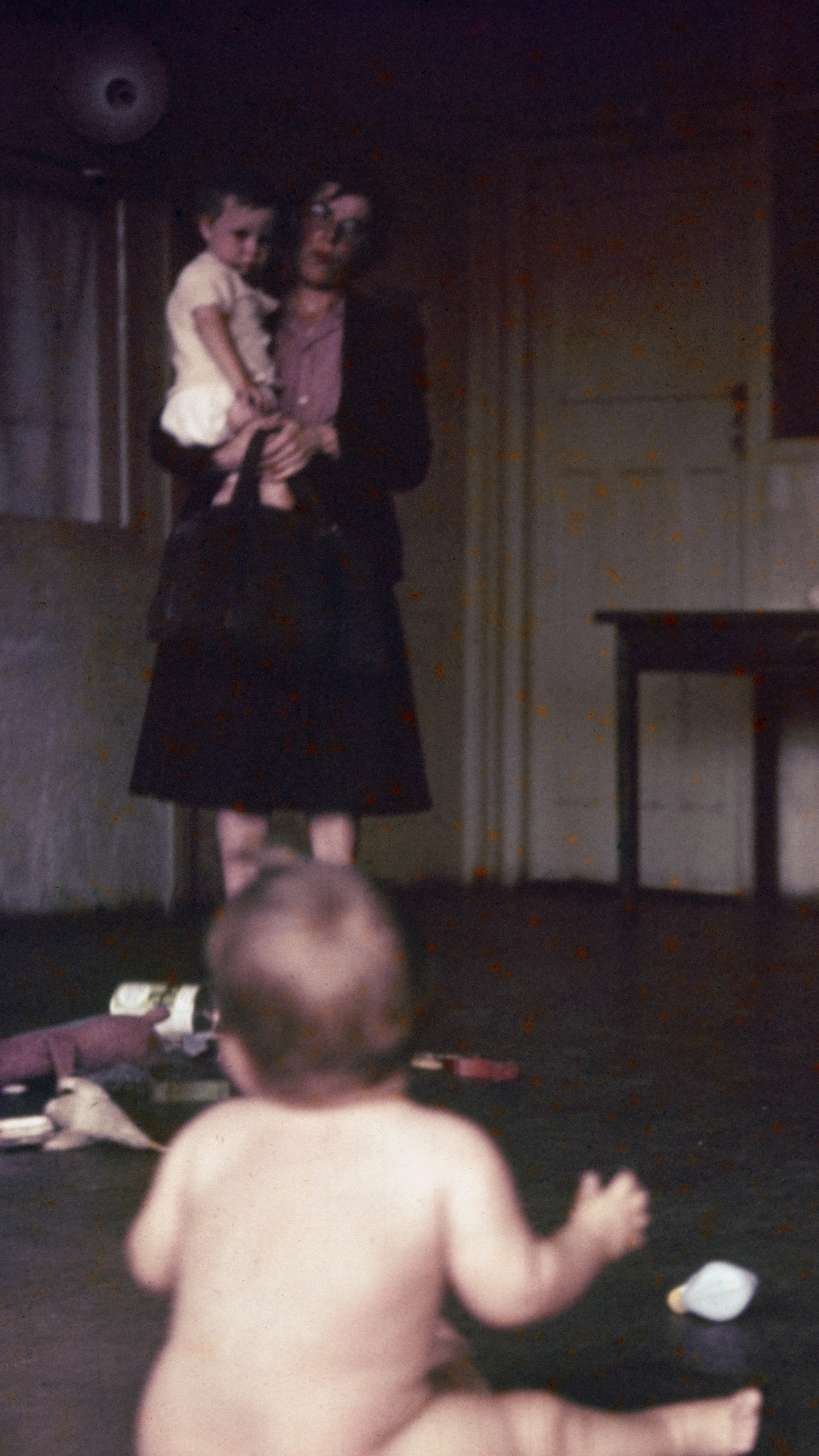 Photograph from the mid-20th Century Peckham Pioneer Centre, showing a woman holding an infant, a large pile of toys, and another infant looking up at her. 