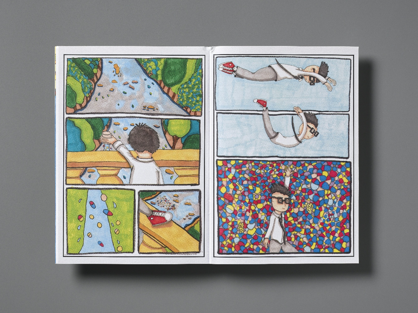 A double page spread of a comic showing, over 7 panels, a young man with thick square glasses looking down onto a river and landscape from a balcony, then jumping off the balcony to fall and land in a mass of multi-coloured pills.