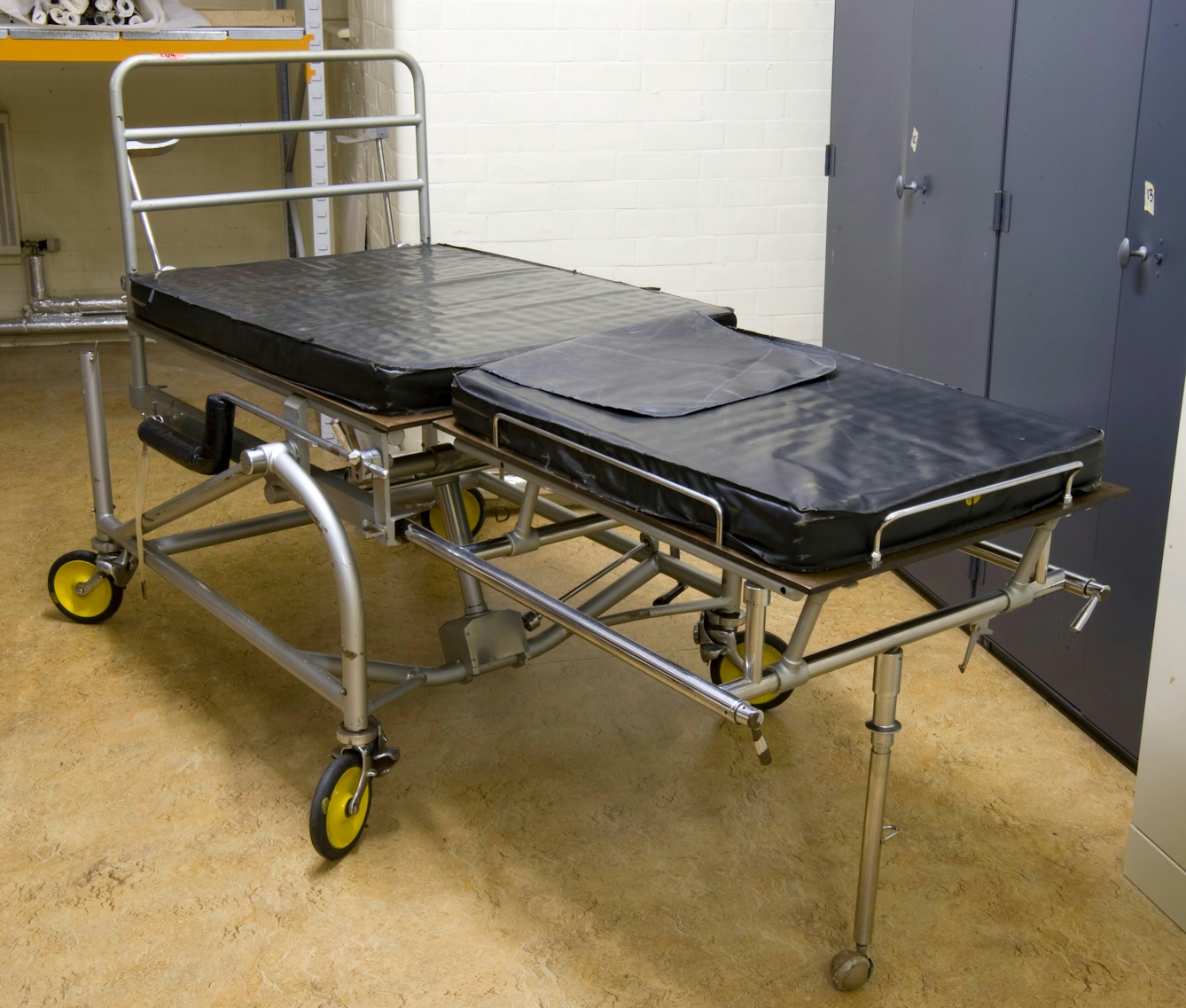 Colour photograph of a delivery table, from between 1945-55. The bed is padded and designed to be fully adjustable and easily cleaned. The main body of the bed sits on four wheels with an extendable section at the foot. 