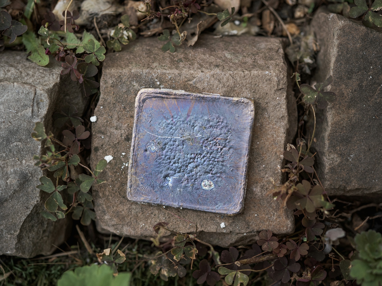 Photograph of a lead plate cooling on a stone. The lead shows signs of lead oxide on the surface, giving off blue and purple colouring.