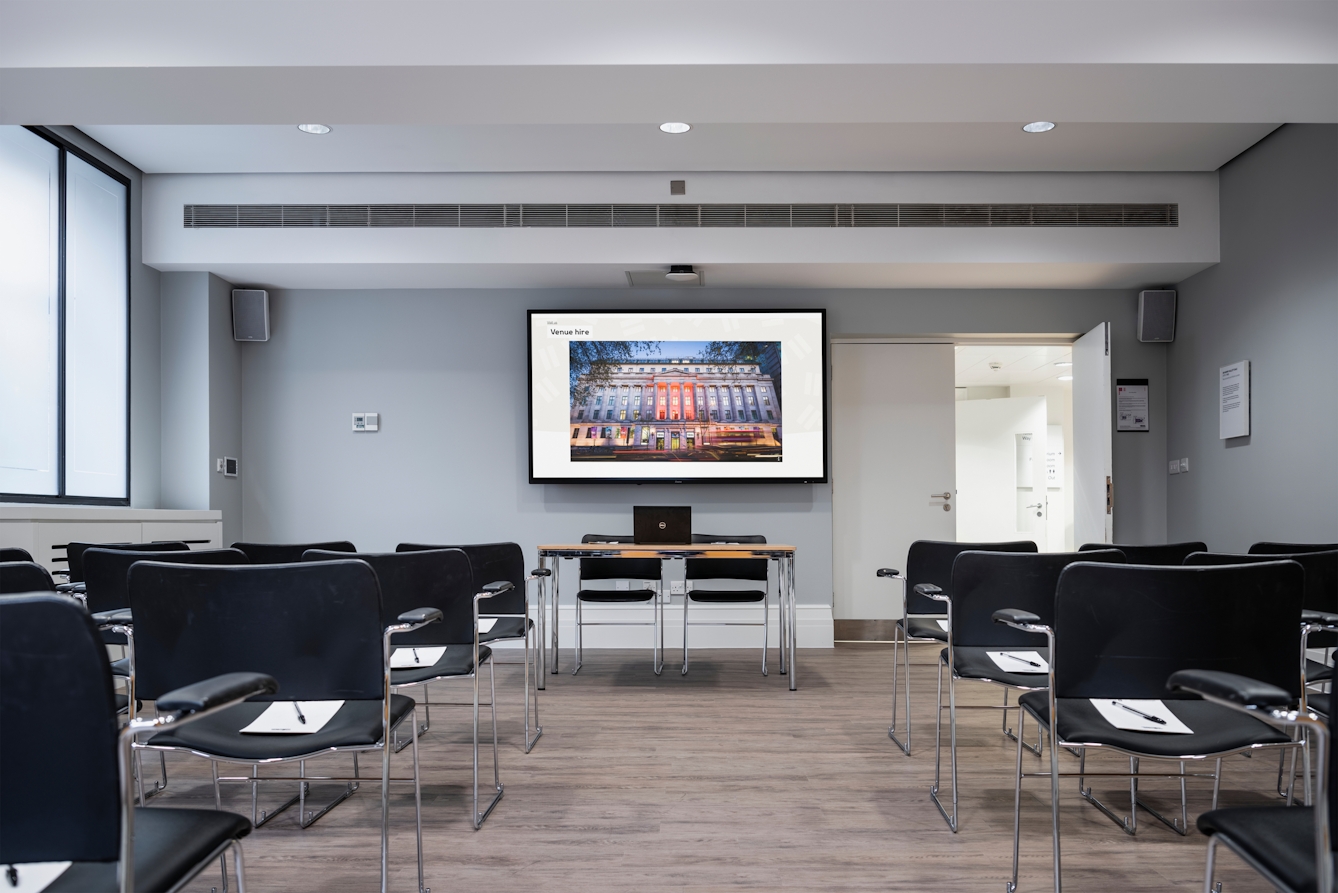 Photograph of the Dale room at the Wellcome Collection. 

Photograph shows a theatre set-up with a desk and presenting screen at the front of the room. 