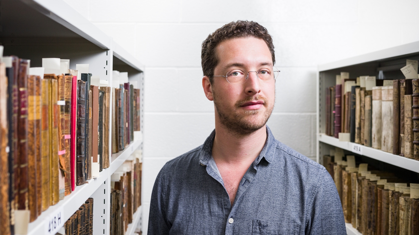 Photographic portrait of Dr. Jack Hartnell in the Wellcome Library's rare book store, flanked on both sides by book cases containing rare and old books.