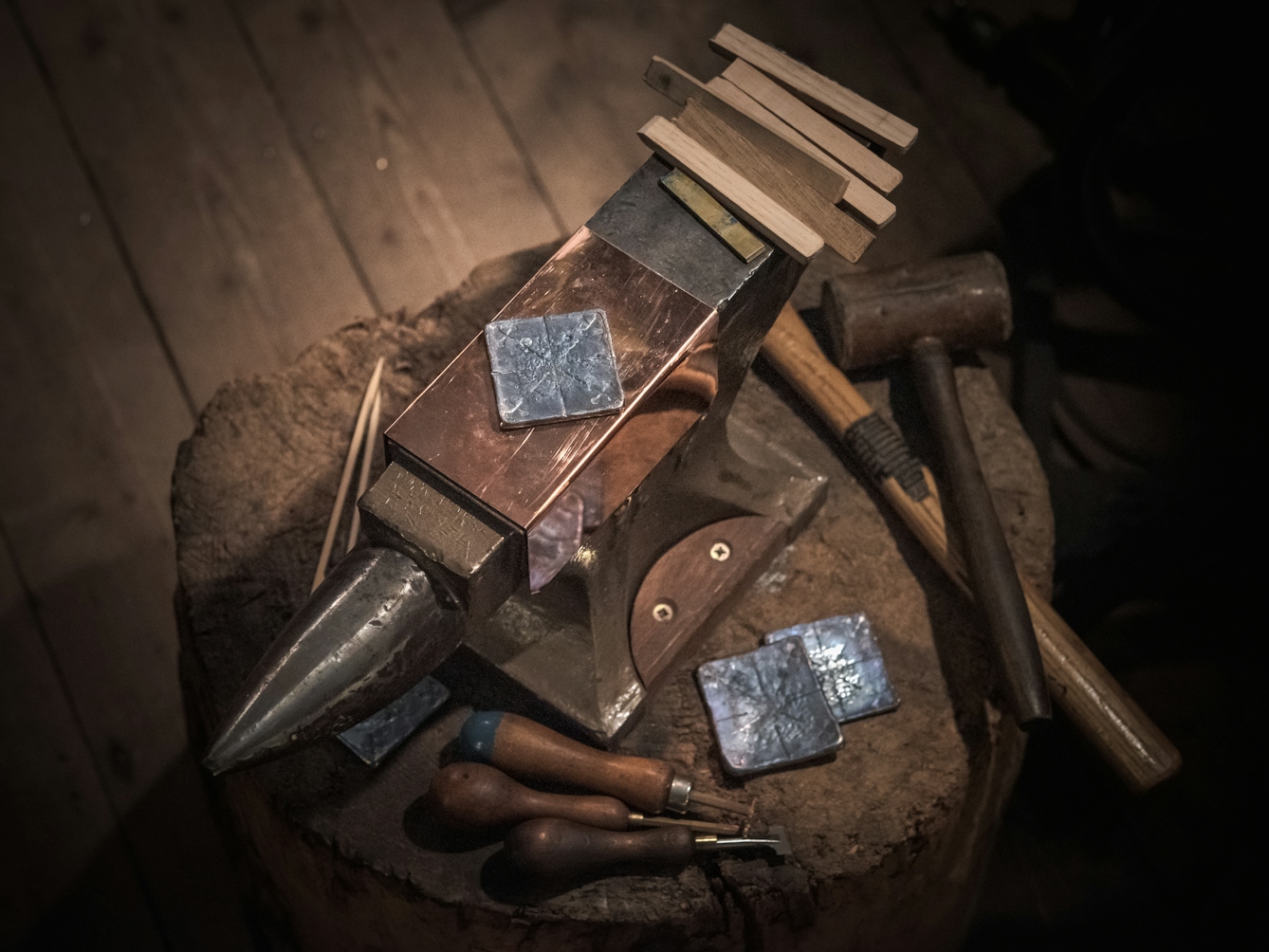Photograph of a lead plate resting on an anvil. Surrounding the lead, to the right, are the tools with which the impressions are made, including specially crafted wooden sticks and a wooden mallet.