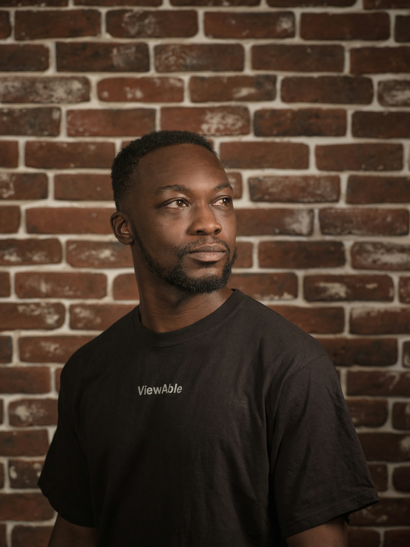 Photographic portrait of a man in a black T-shirt with the word 'Viewable'.  The man is facing to the right of the frame, and gazing into the middle distance.