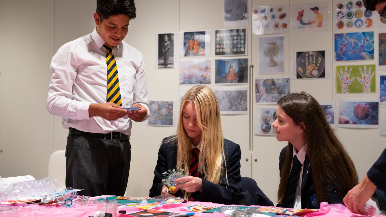 A group of school children sitting and standing around a table with art materials on it.