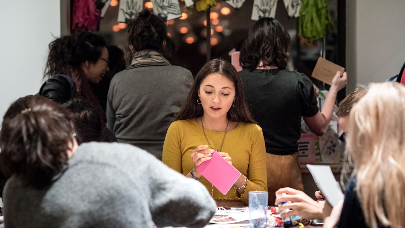 A group of people sitting around a table covered with paper engaged in crafting activities and making zines.