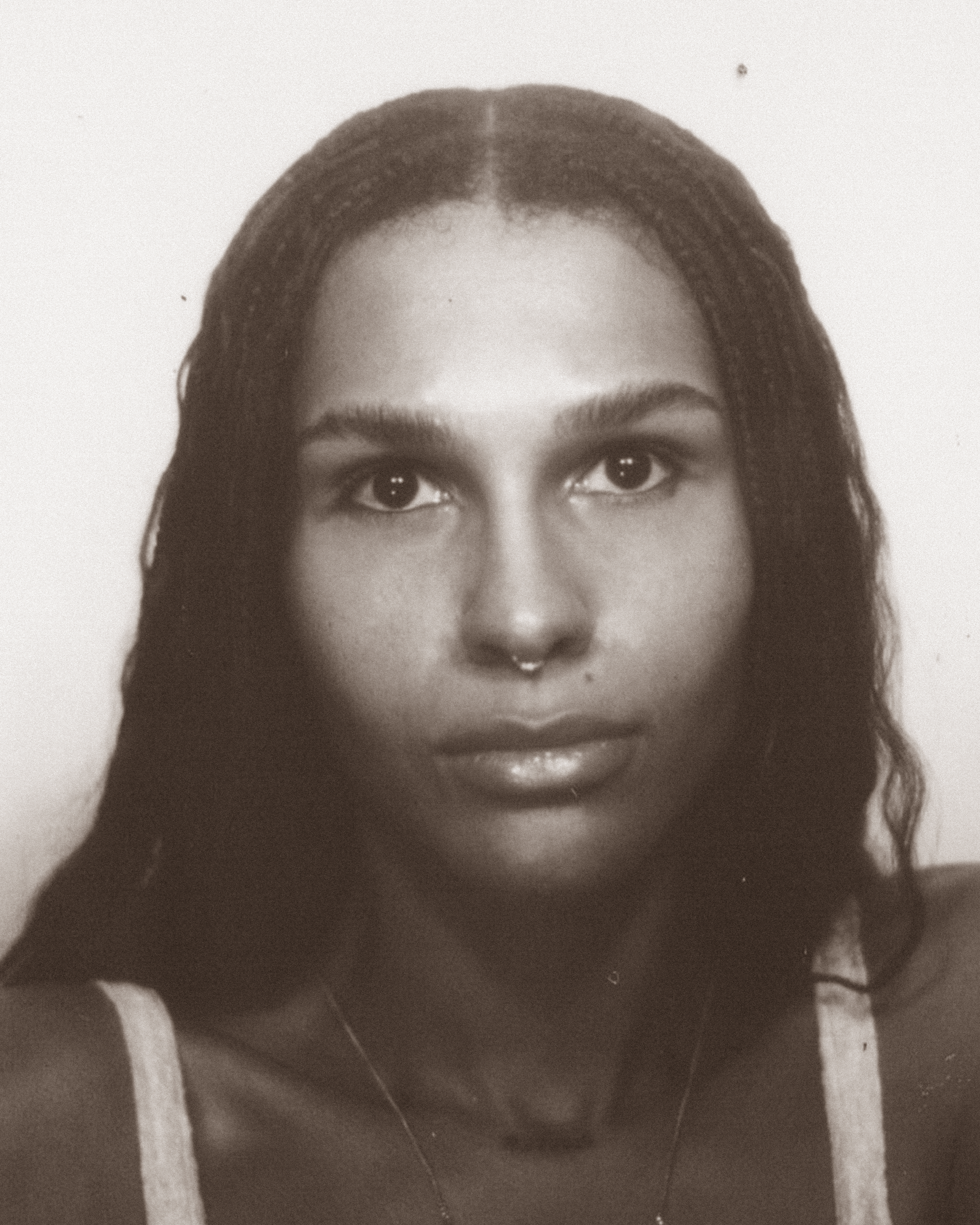 Black-and-white headshot of a person with long, centre-parted hair and a septum piercing, looking directly at the camera.