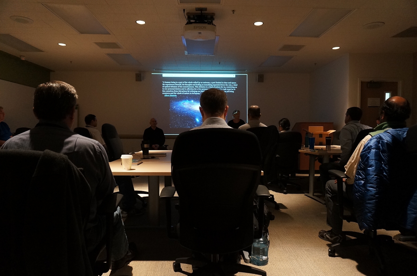 People sitting in chairs before a projector screen depicting a picture of a galaxy.