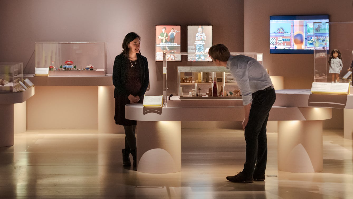 Visitors at the Play Well exhibition at Wellcome Collection. Two people are looking at items in a case.
