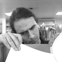 Black and white photograph of a man with dark hair peering into a box of documents.