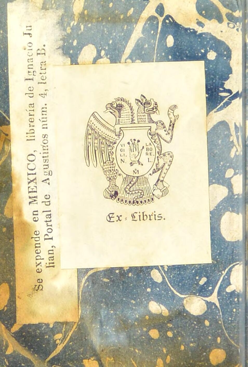 Bookplate pasted on the inside cover of a book, featuring the words 'Ex Libris' and an image of two fierce creatures, possibly a bird of prey and a big cat, behind an urn with an image of a hand and a set of initials on it.  To the left of the bookplate and parallel to the long outer edge of the inside cover, is pasted a slip of paper with the words 'Se expende en MEXICO, libreria de Ignacio Ju lian, Portal de Augustinos num. 4, letra B.'