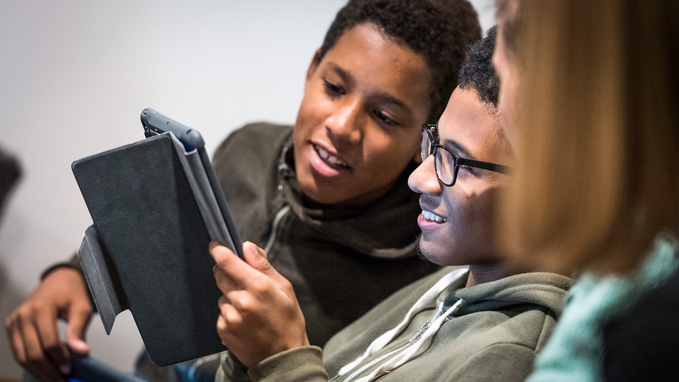 Photograph of two young school boys smiling and looking at a tablet screen, involved in a class learning activity.