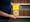 Photograph of the midriff of a man who is holding a pamphlet titled 'Dial a Drug - what you should know about drugs and drug abuse'. In the background are a set of out of focus shelves containing books.