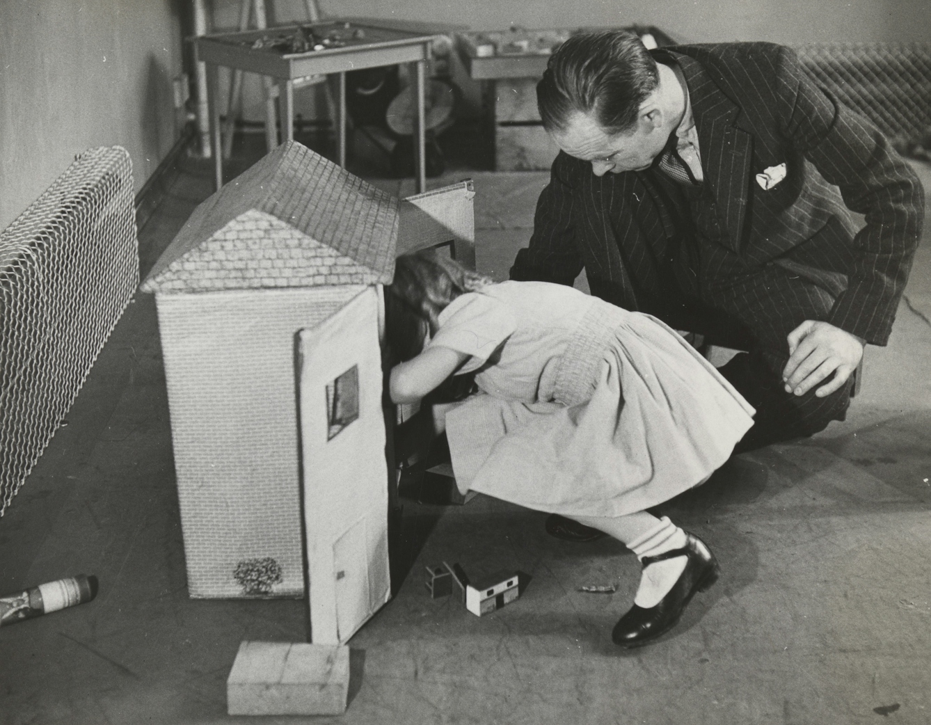 A man looks into a doll's house with small child.