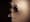 Photograph of a brown membrane with the edge of a door with latch and handle appearing in relief through it. Clasped around the edge of the door are two skeletal hands. To the right of the hands the form of a face and head appear through the membrane, mouth wide open.