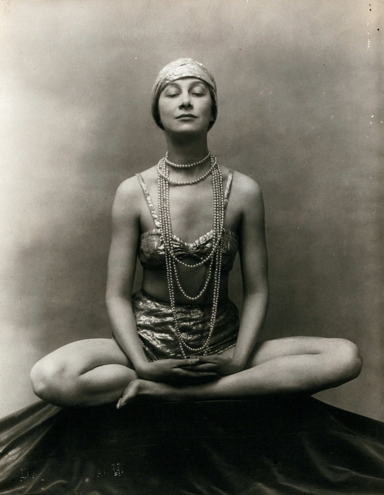 A woman in 1920s dres seated in the Buddha Pose