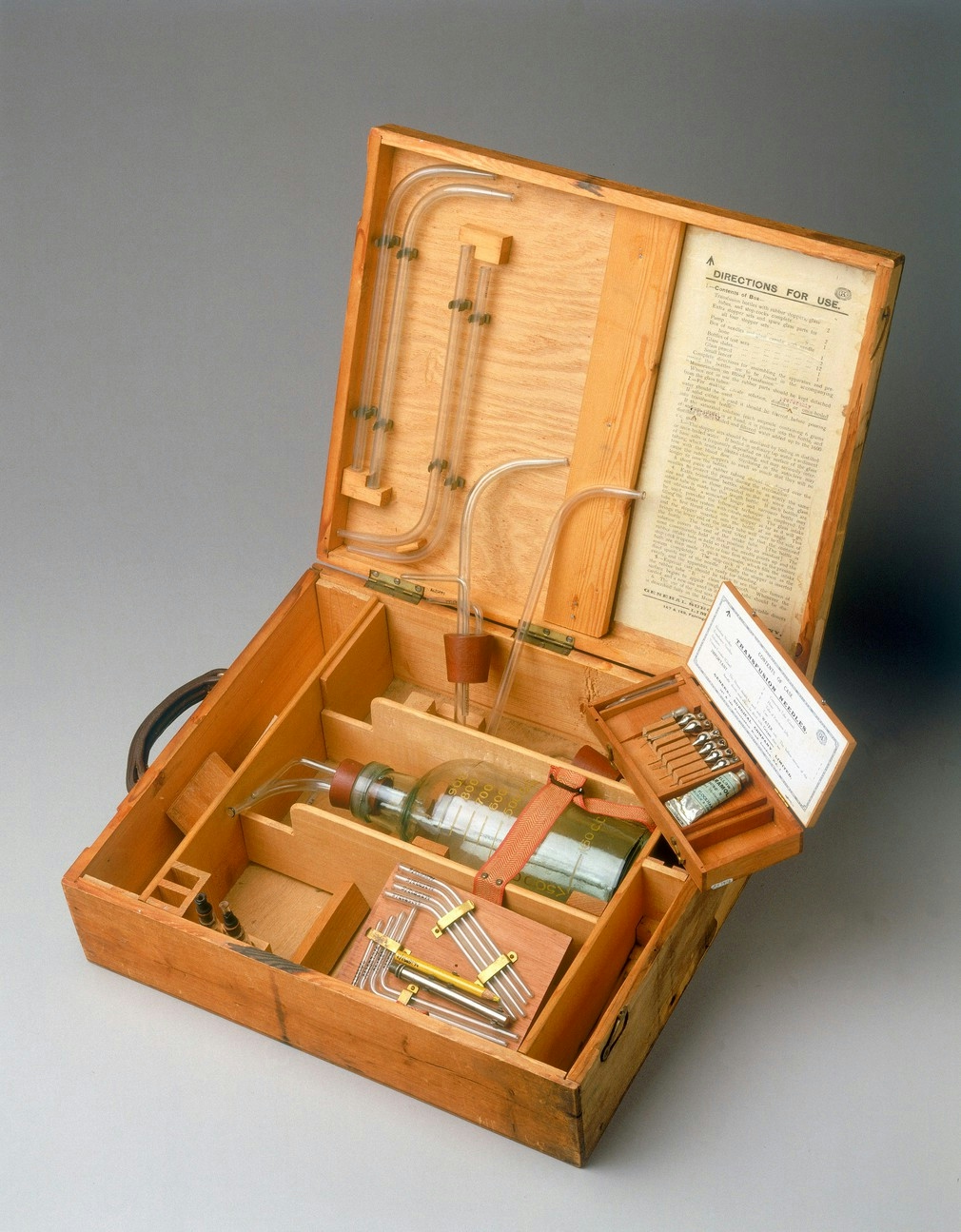 Image of an open wooden box with section dividers containing tubes and a bottle.