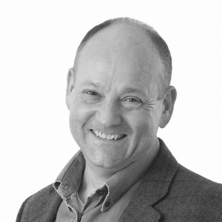 Black and white, head and shoulder photograph of a man with short hair wearing a shirt and jacket. 
