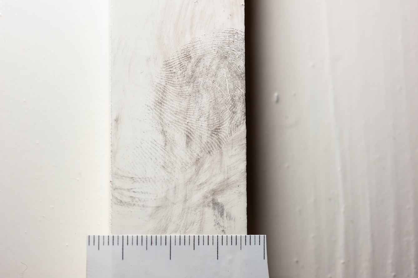 Photograph of a dusted fingerprint on a white door frame with a ruler scale beneath. 
