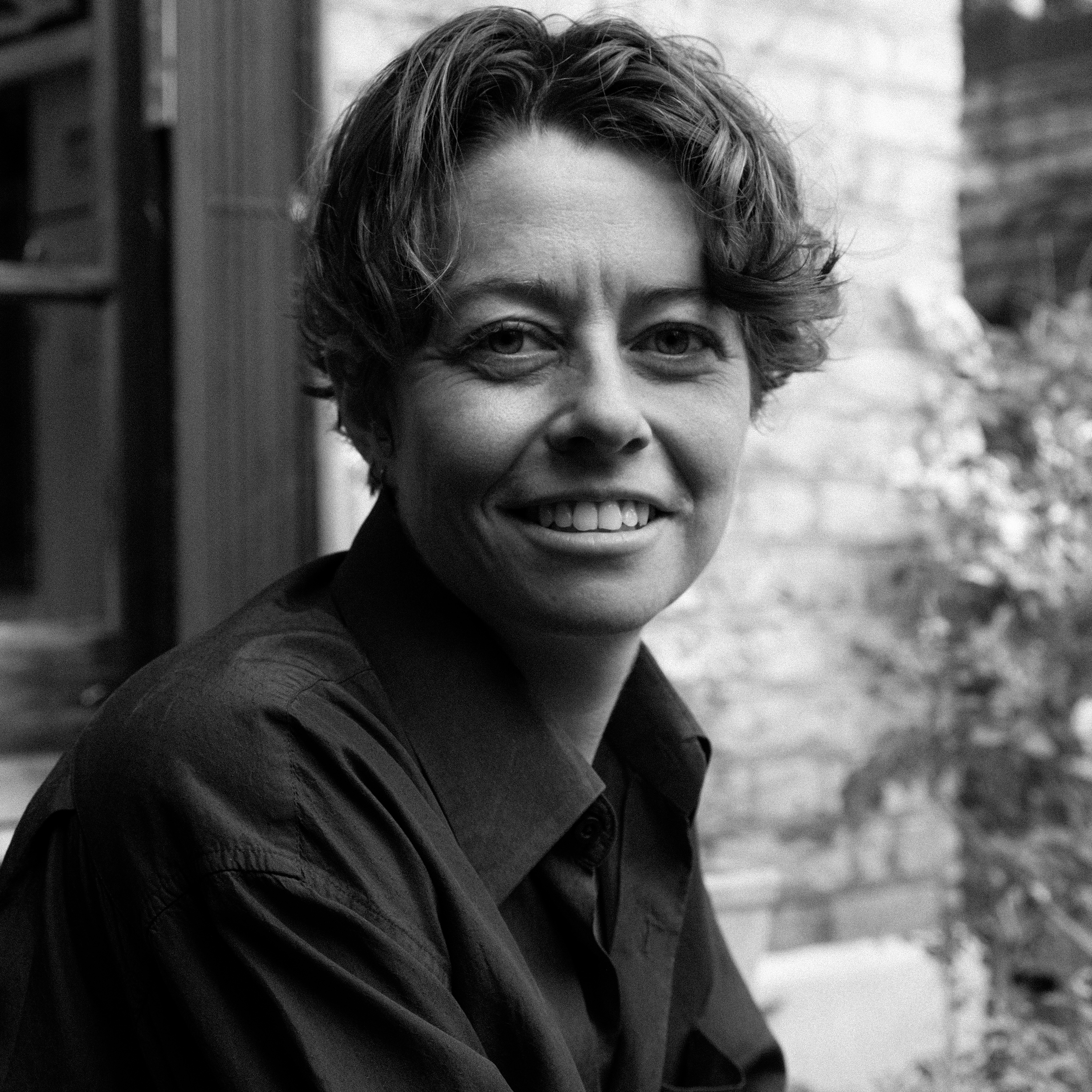 Black-and-white headshot of a person with short, wavy hair, wearing a dark collared shirt.