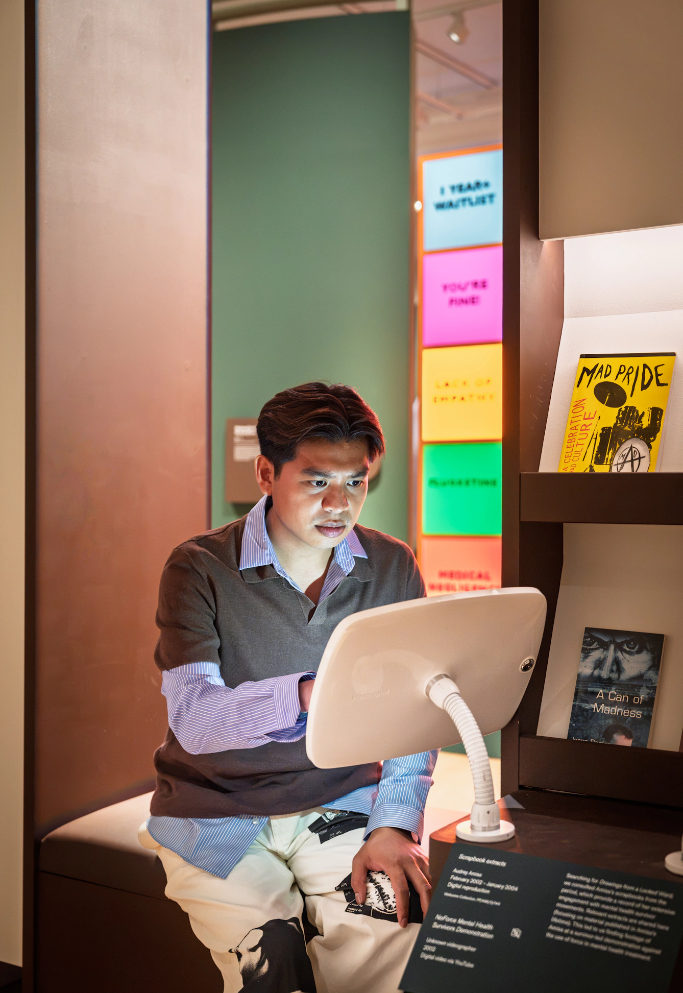 Photograph of a gallery visitor sitting on a bench seat exploring content on an tablet device, secured in a case.