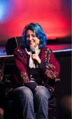 Black and white photo of a young person seated in a wheelchair and holding a microphone. 