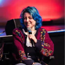 Black and white photo of a young person seated in a wheelchair and holding a microphone.
