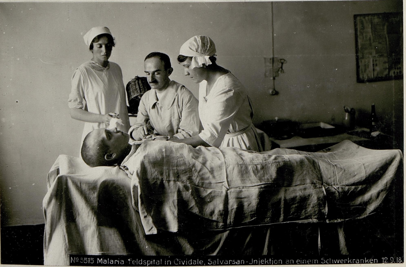 Black-and-white photograph of a patient lying on a hospital bed while three medical staff administer an injection. The patient is covered with a sheet.