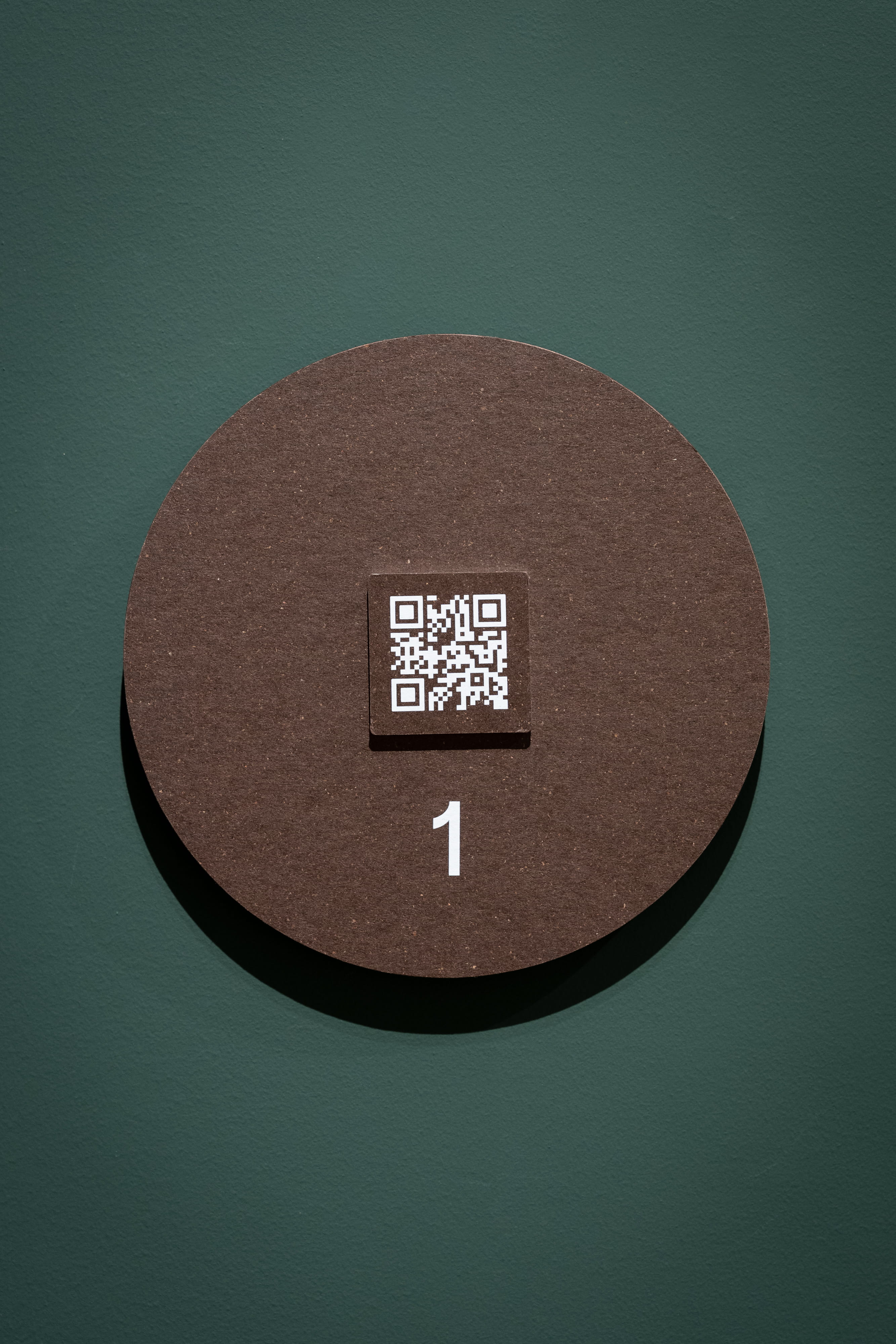 Circular marker with a QR code and the number 1, mounted on a dark green wall.