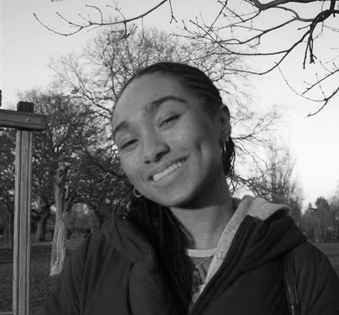 Black and white photo of the head and shoulders of a young woman. Her head is tilted to one side, she is smiling and looking at the camera.