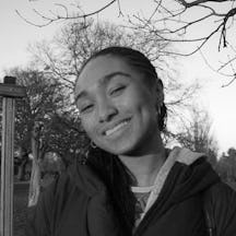 Black and white photo of the head and shoulders of a young woman. Her head is tilted to one side, she is smiling and looking at the camera.