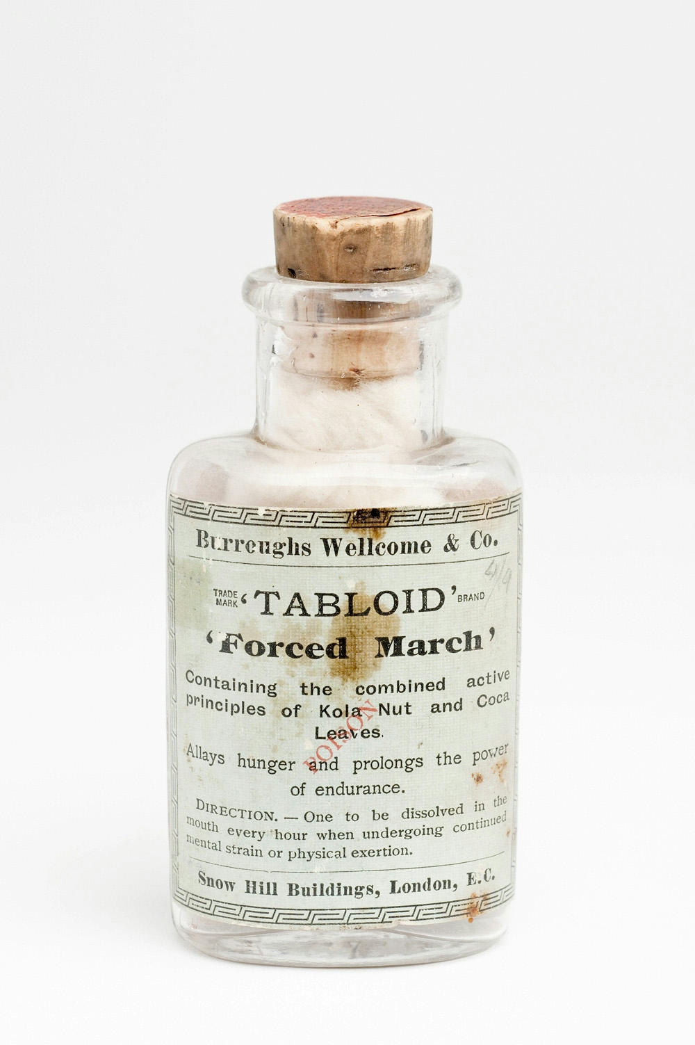 A clear glass bottle with cork stopper. The label on the bottle says: "Burroughs Wellcome & Co. 'TABLOID' 'Forced March'. Containing the combined active principles of Kola nut and Coca leaves. Allays hunger and prolongs the power of endurance. Direction - one to be dissolved in the mouth every hour when undertaking continued mental strain or physical exertion."