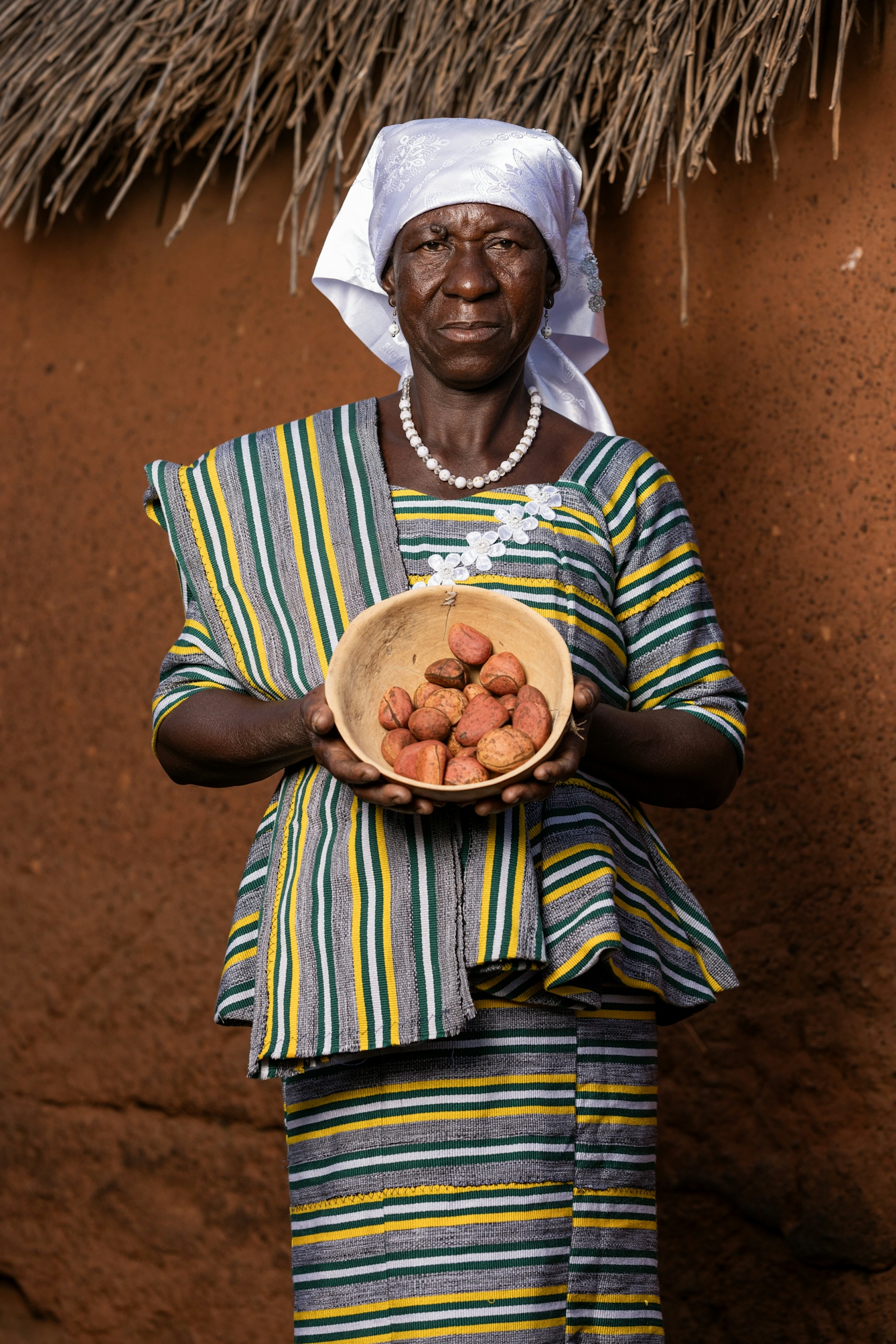 A Ghanaian person wearing patterned clothing holding a bowl containing several individual kola nuts.