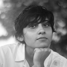 Black and white photograph of the head and shoulders of a young woman with short black hair. She is looking at the viewer, with their chin resting on ther fist.
