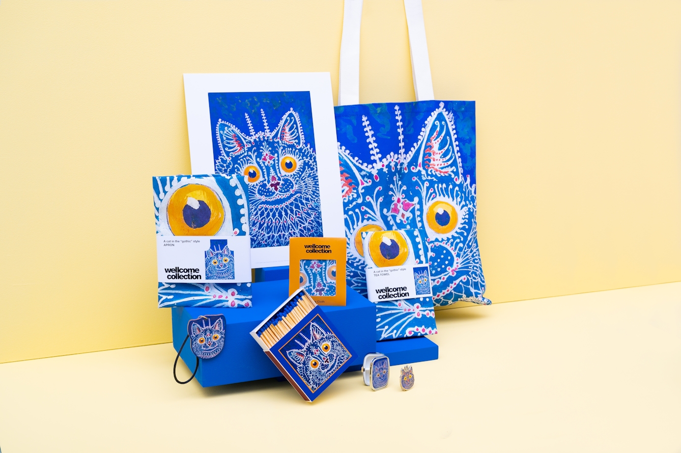 A series of small podiums. On the podiums are gifts and merchandise: a print, tote bag, tea towel, apron, matches, pin and key chain with the image of a cat.