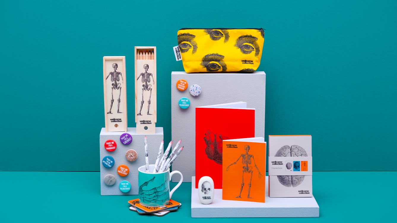 A series of small podiums decorated with badges. On the podiums are gifts and merchandise: notebooks, pencils, a rubber and mug with the image of a brain, skeleton or heart. A makeup bag with the image of eyes sits atop the highest podium.