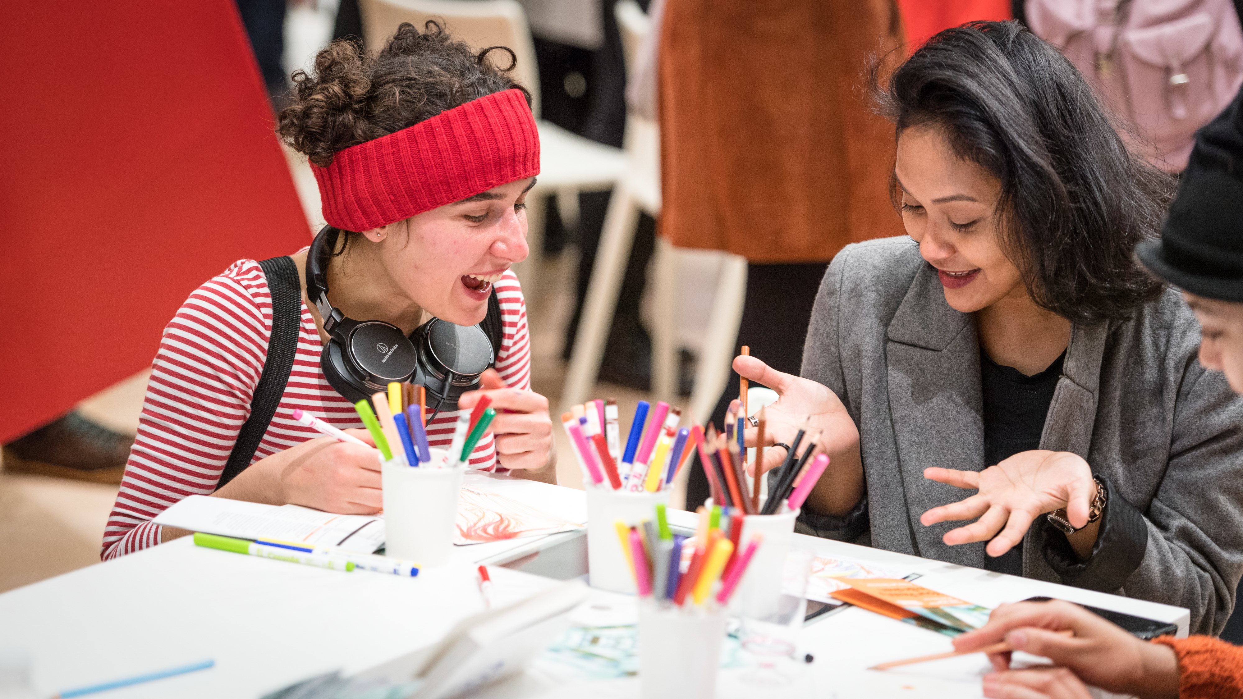 Photograph of two women sat at a table surrounded by coloured pens and pencils, undertaking a creative drawing workshop.