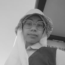 A young person wearing large round glasses and a hat and scarf on ther head. They are looking down into the camera.