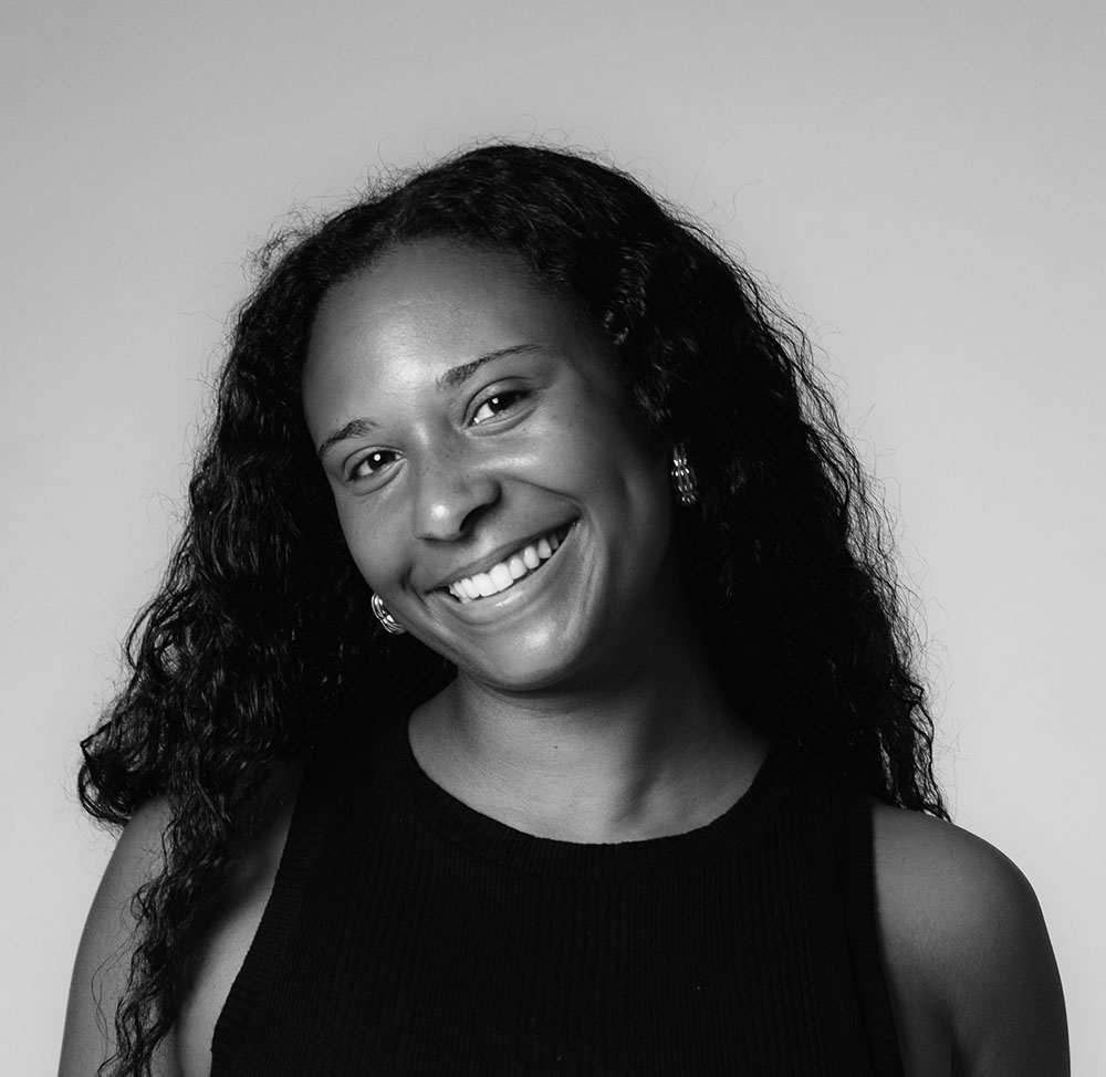 Black and white photograph of the head and shoulders of a young black woman with long hair. She is smiling and looking directly at the camera.