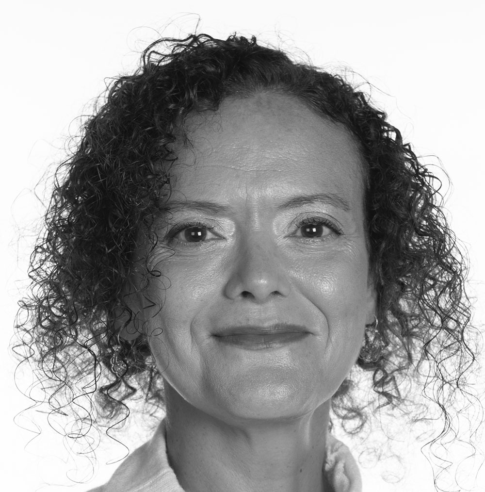 Black and white photograph of the head of a middle-aged woman with short curly hair. She is smiling and looking directly at the camera.