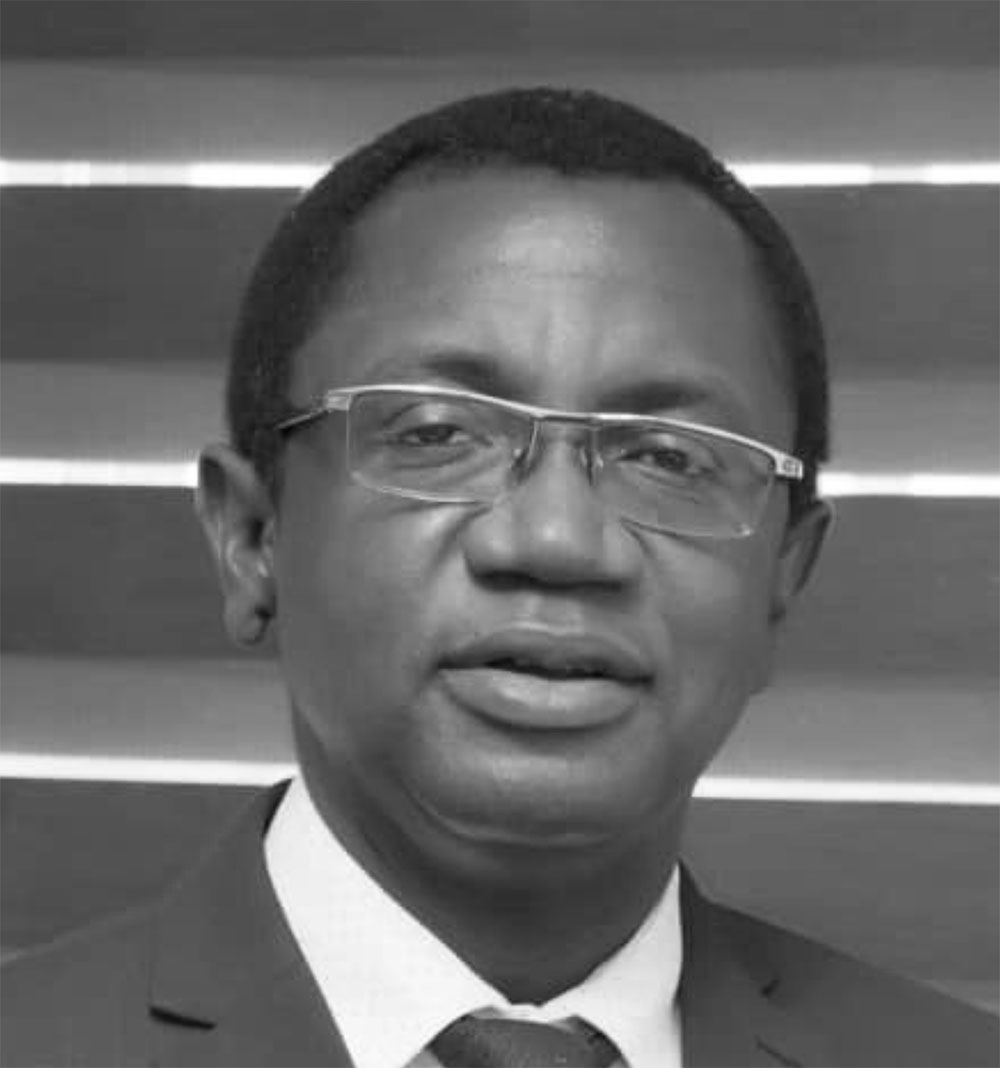 Black and white photograph of the head and shoulders of a middle-aged man wearing glasses. He is looking directly at the camera.