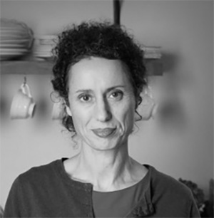 Black and white photograph of the head and shoulders of a middle-aged woman. She is looking directly at the camera.