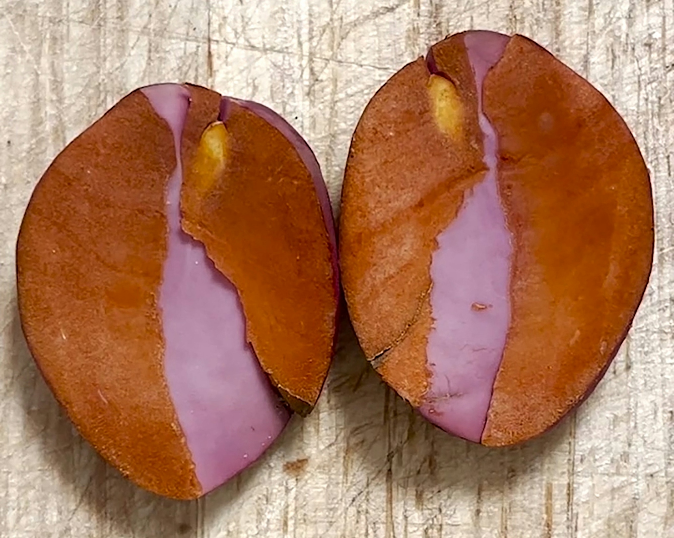 A photograph from a film of an oval nut that has been cut in half and is transitioning from pink to orangey-brown in colour.