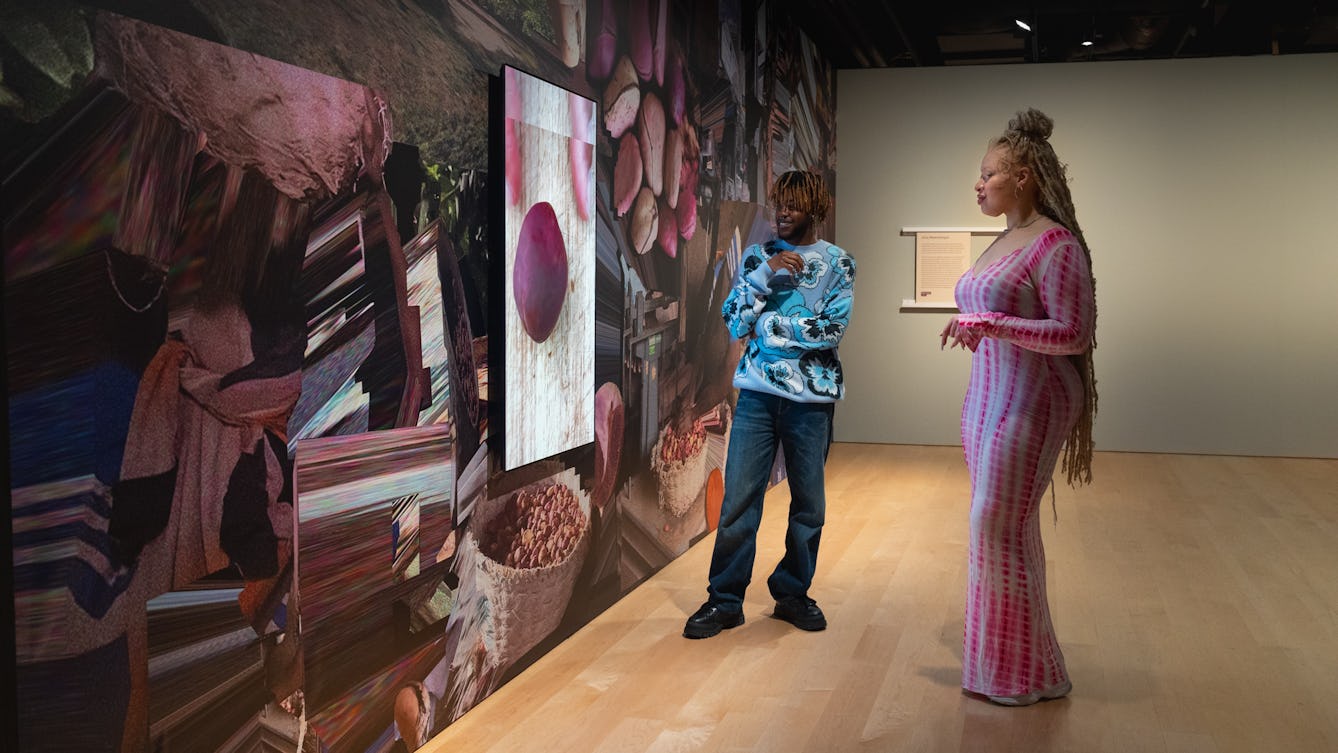 Photograph of two gallery visitors watching a short film in a gallery setting.