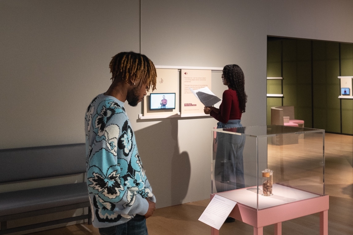 Photograph of a gallery visitor watching and listening to a BSL-interpreted video in a gallery setting.