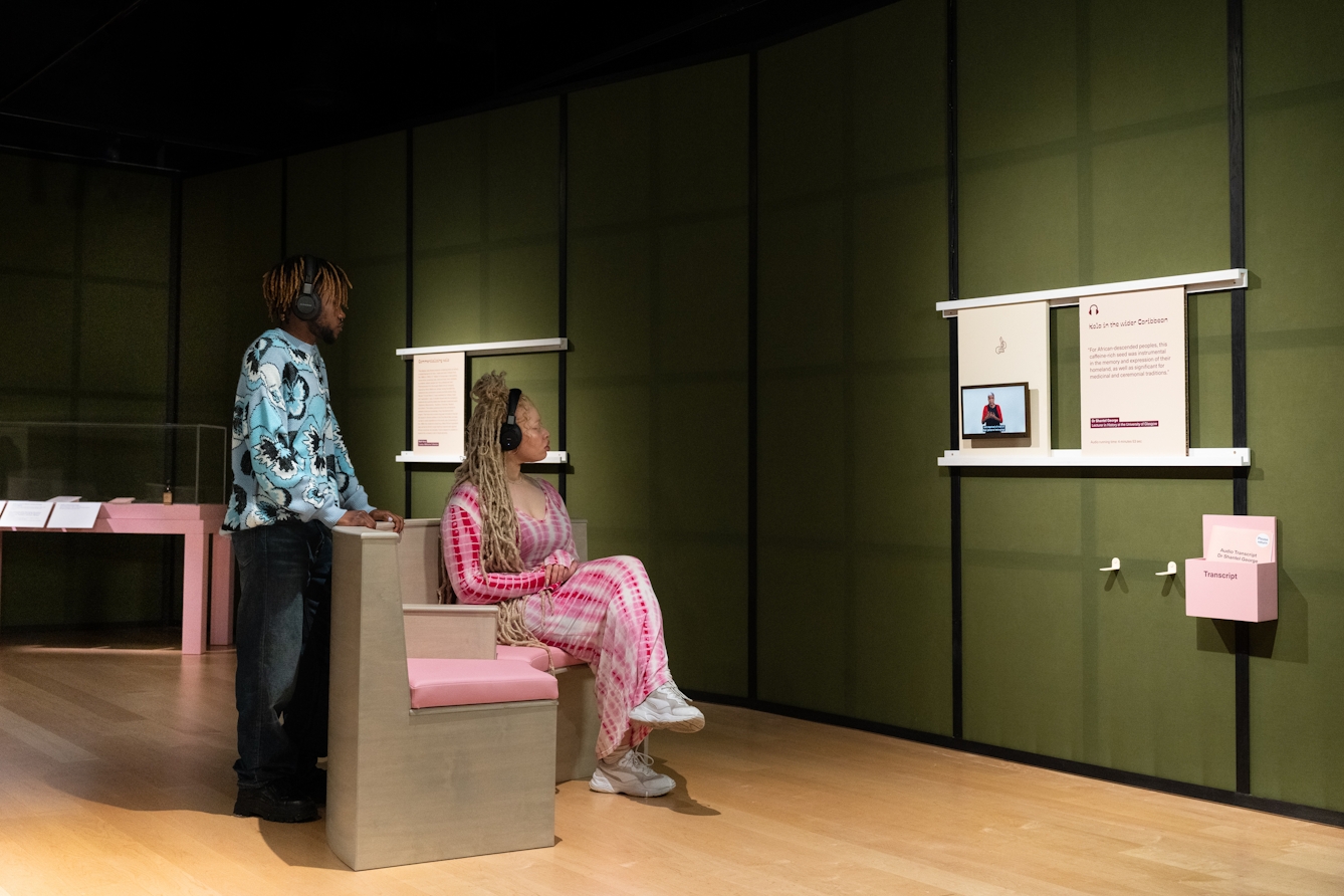 Photograph of two gallery visitors watching and listening to a a BSL-interpreted video in a gallery setting.