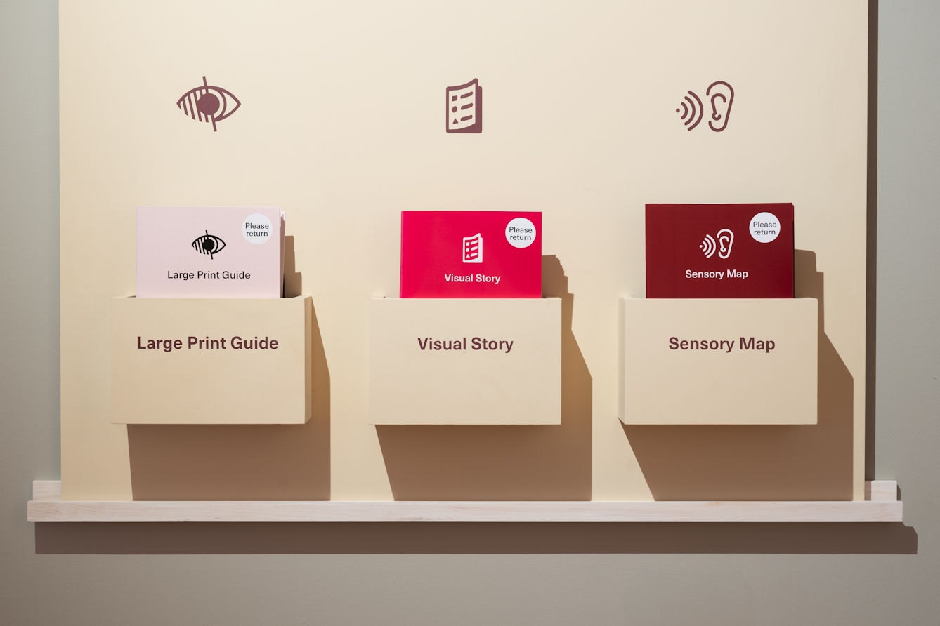 Photograph of three shelves housing the large print guides, visual story and sensory map for the exhibition 'The Kola Nut Cannot be Contained'.