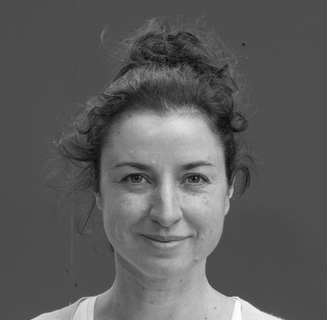 Black and white photo of the head and shoulders of a young woman with her hair in a tight bun. She is smiling and looking directly at the viewer.